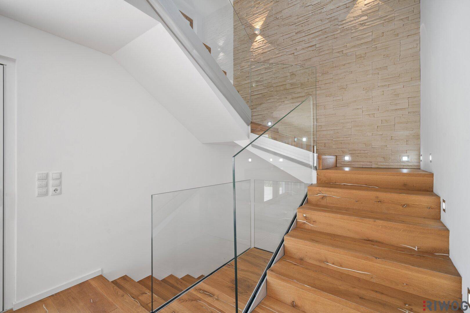 Moderne Holztreppe mit Glasgeländer und dekorativer Steinwand, die das Treppenhaus aufwertet.