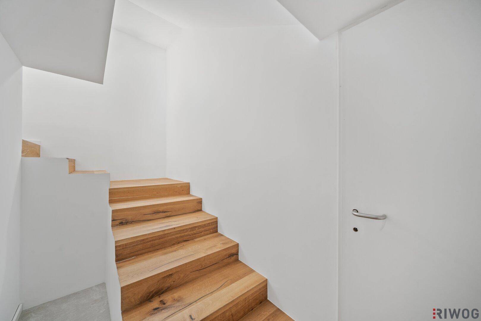 Schlichte Holztreppe mit weißen Wänden, die in das obere Stockwerk führt.