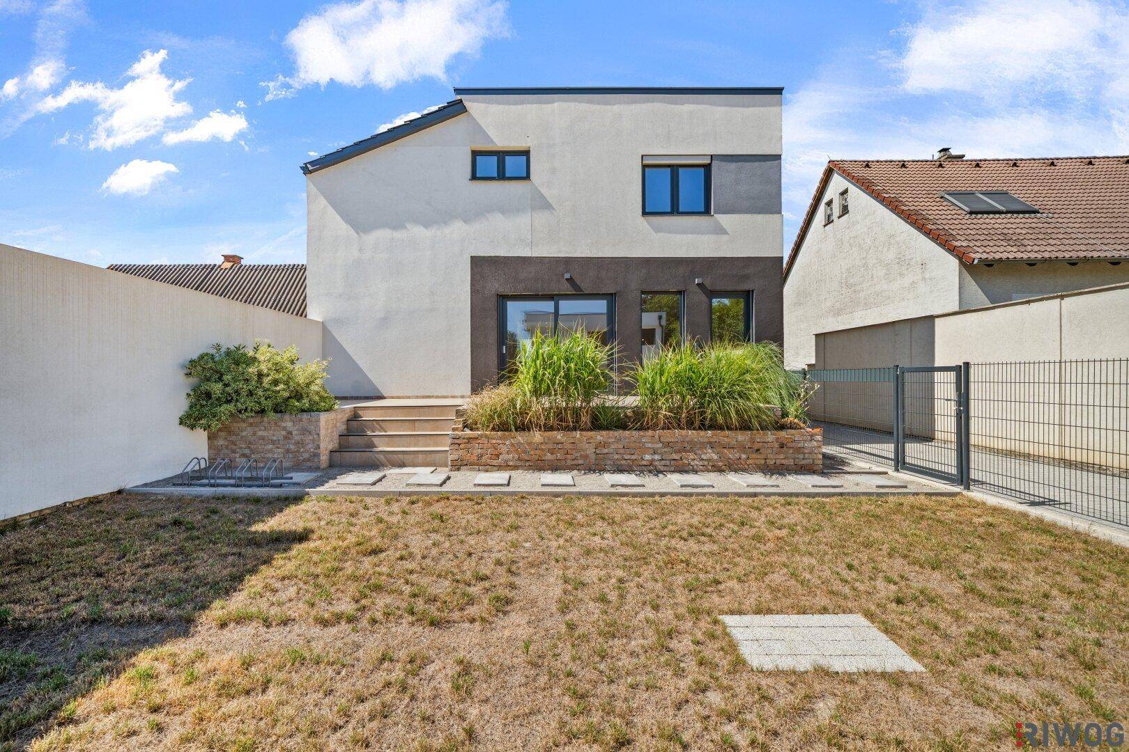 Rückseite eines modernen Hauses mit großem Garten und Zugang zur Terrasse über Stufen.