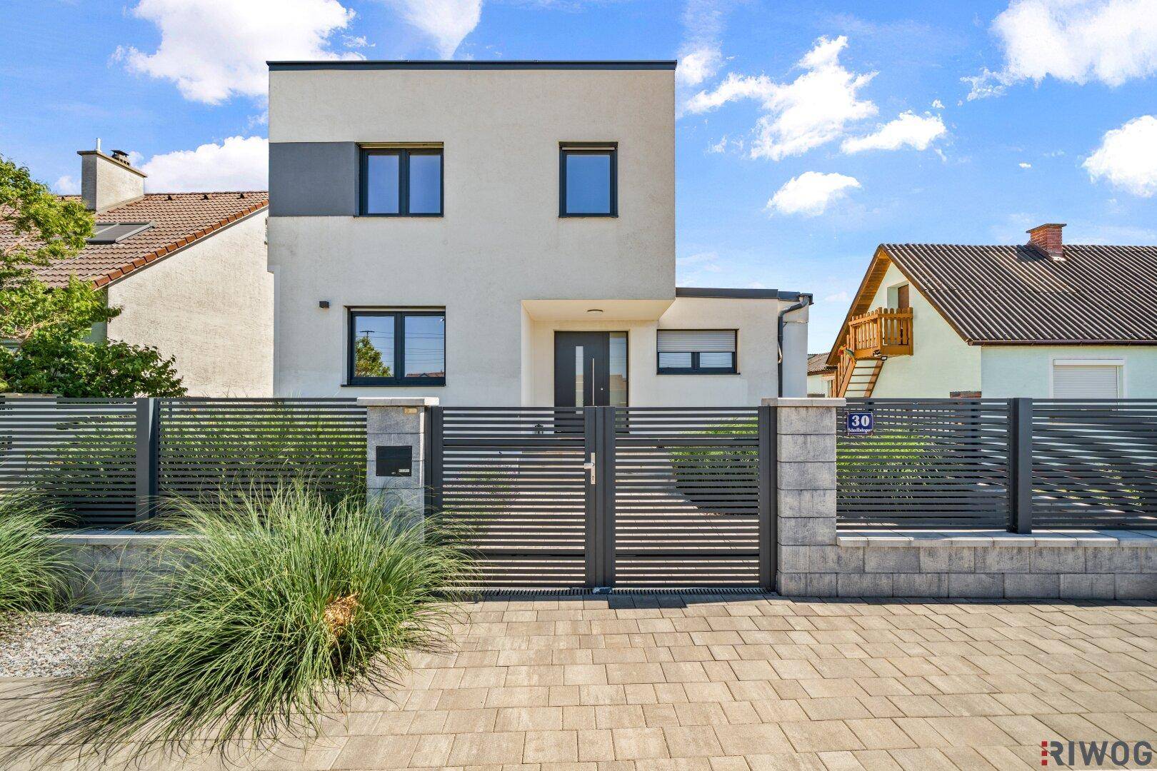 Moderne Hausfassade mit klaren Linien, großen Fenstern und einem gepflegten Vorgartenbereich.