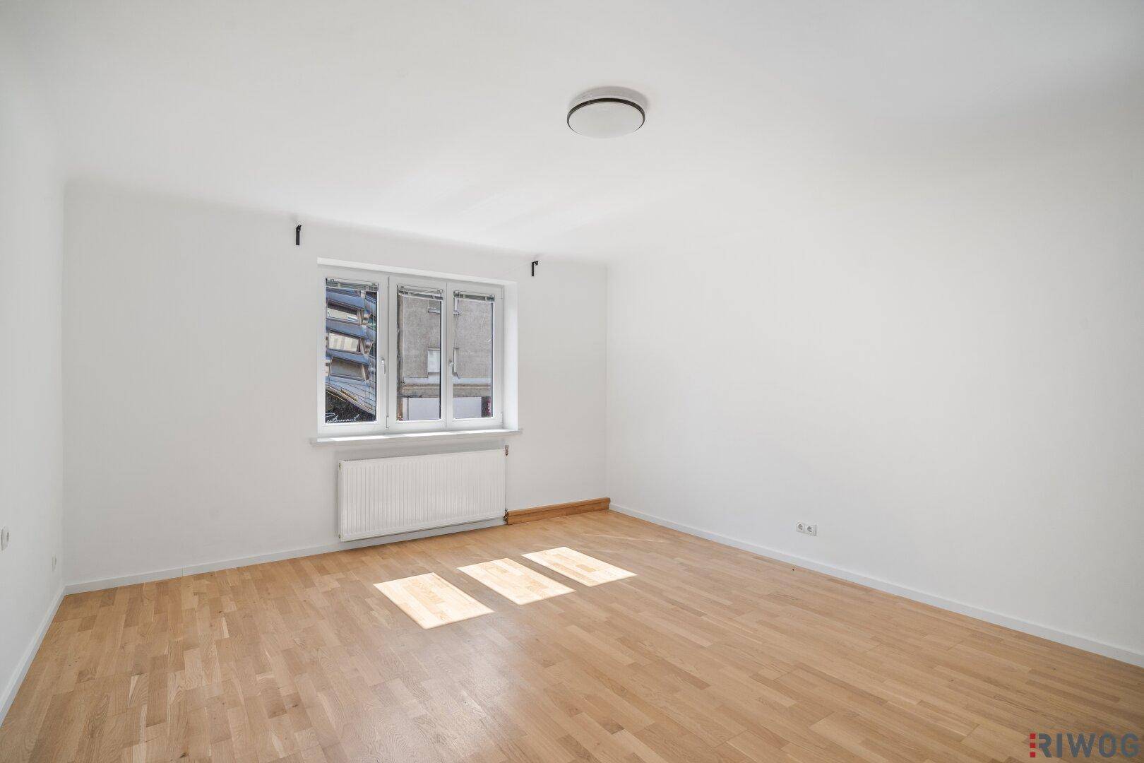Geräumiges Zimmer mit hellem Parkettboden und viel Tageslicht durch das Fenster.