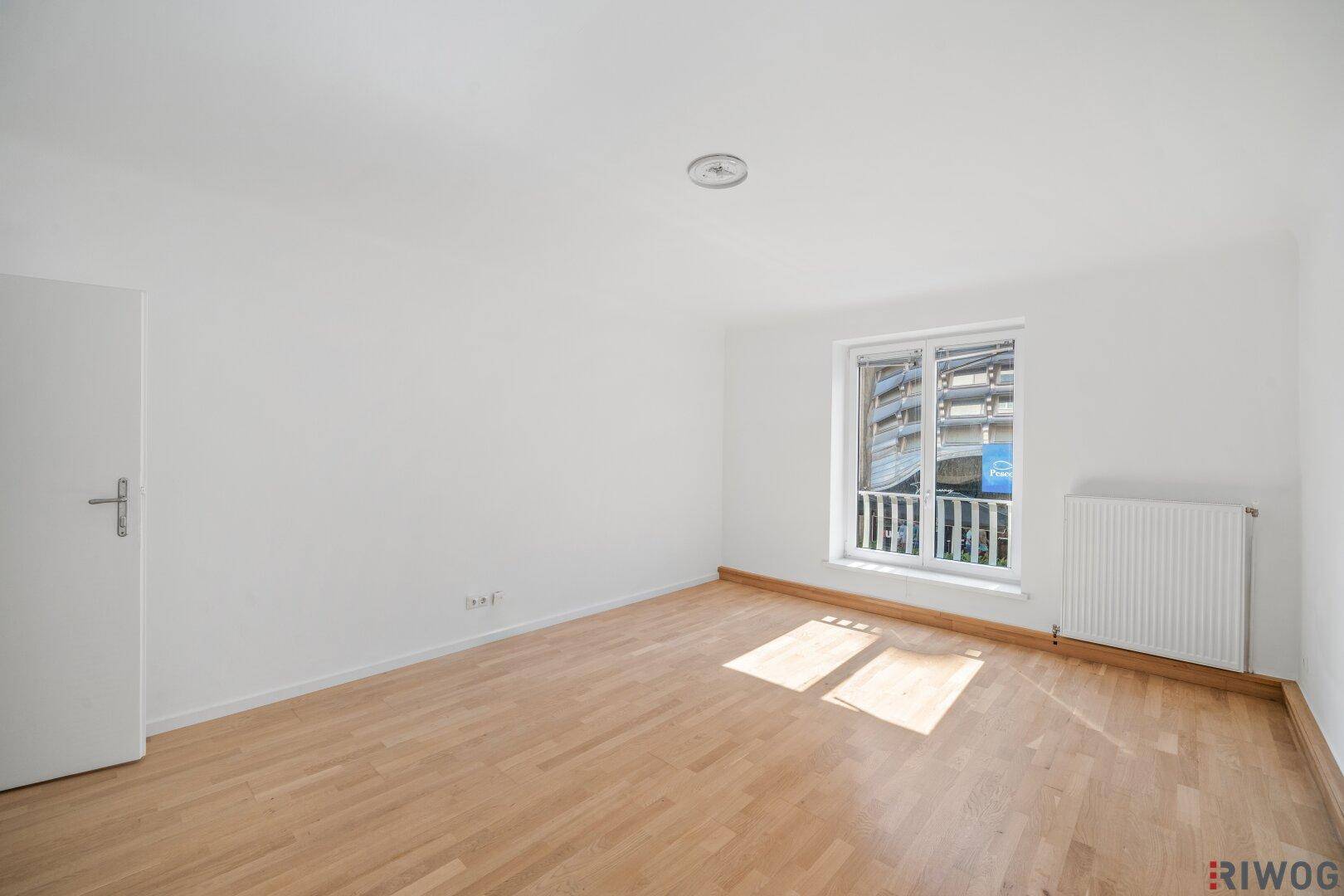 Lichtdurchflutetes Zimmer mit Parkettboden, weiß gestrichenen Wänden und französischem Balkon.