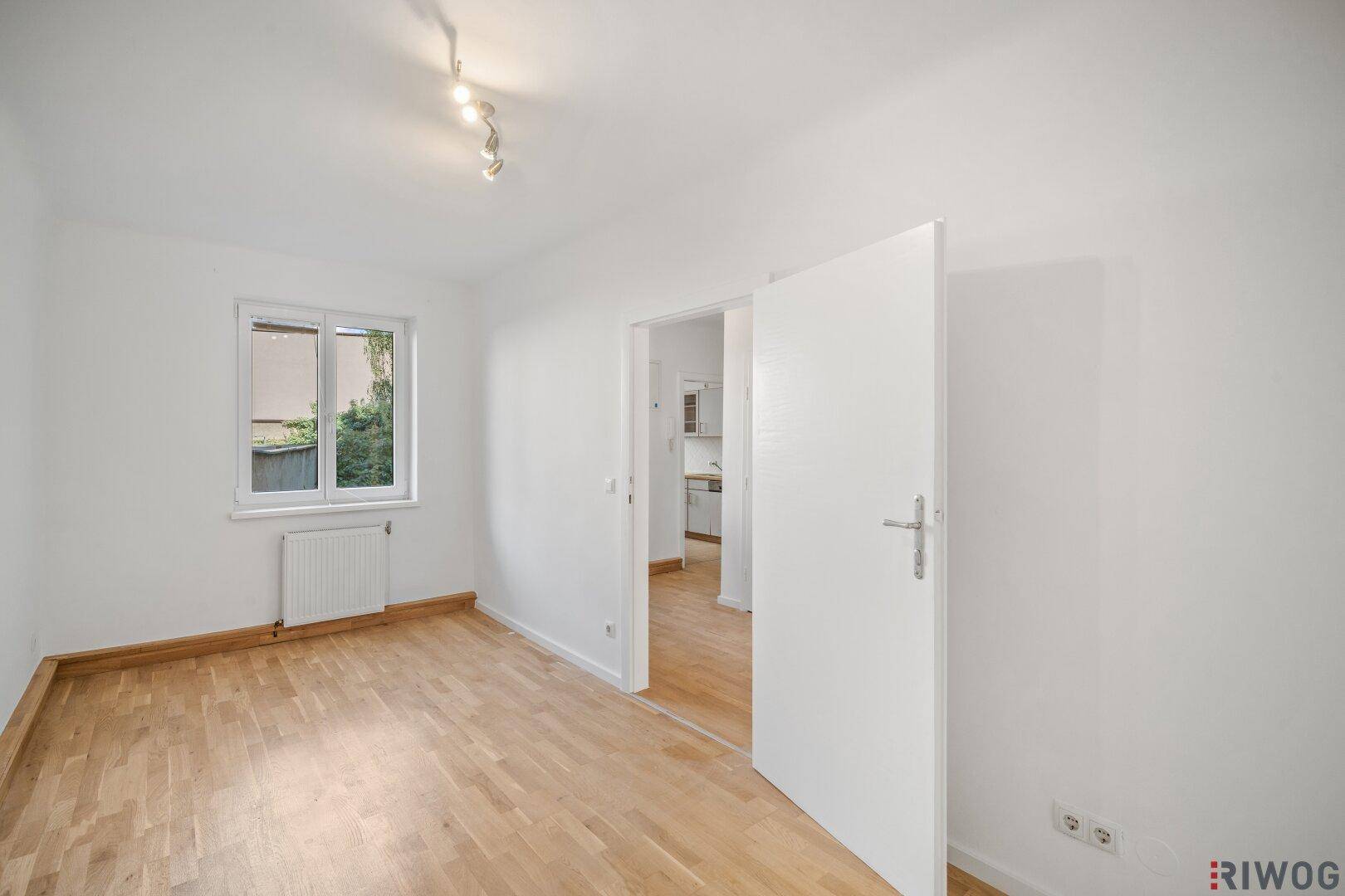 Helles Zimmer mit Parkettboden und Zugang zu einem weiteren Raum, ideal für flexible Nutzung.