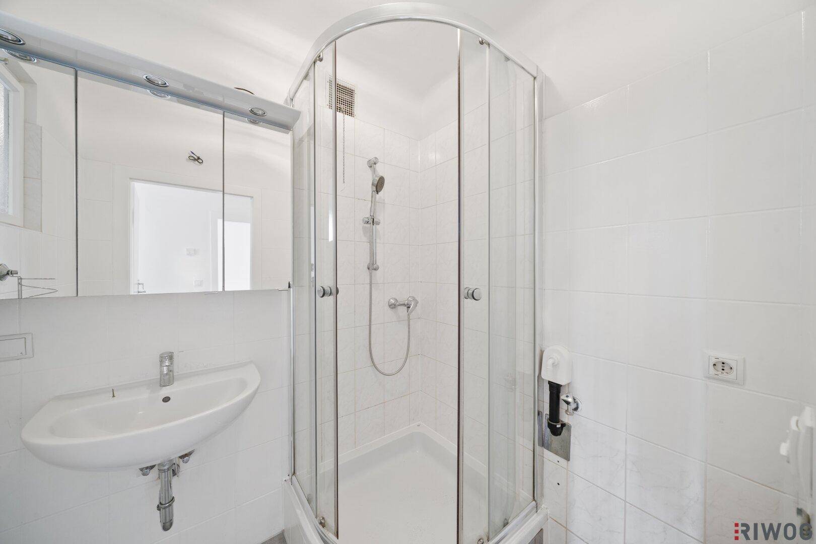 Modernes Badezimmer mit weißer Fliesenverkleidung, Duschkabine und Waschbecken.