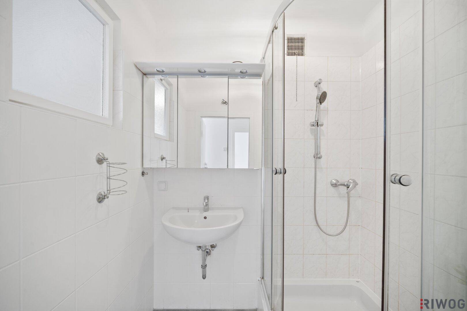 Helles Badezimmer mit weiß gefliesten Wänden, Duschkabine und Spiegelschrank.