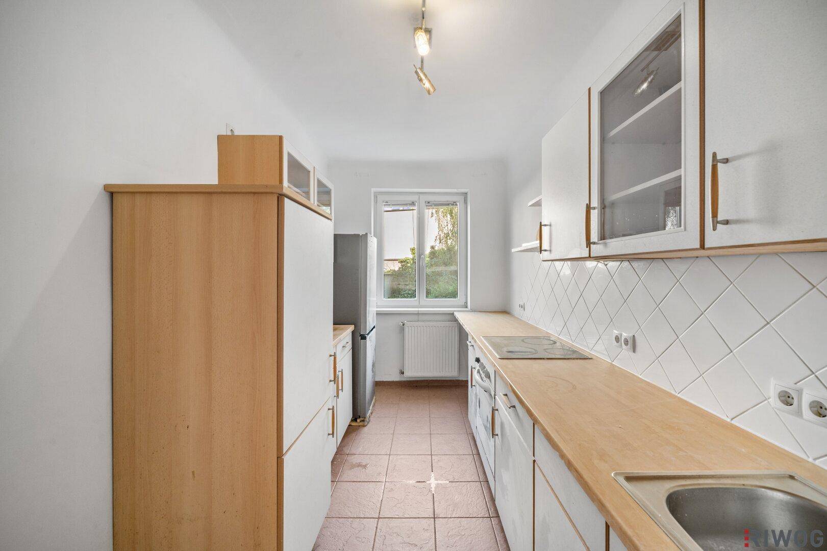 Praktische Küche mit weißen Unterschränken, Holzarbeitsplatte und Fenster mit Grünblick.