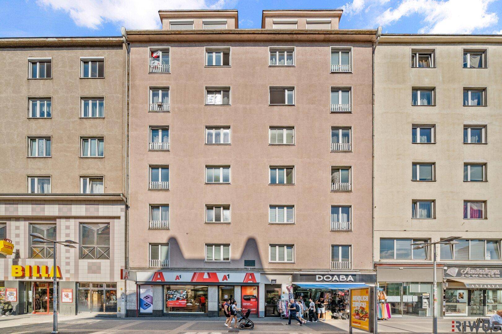 Fassade eines Mehrfamilienhauses mit Geschäften im Erdgeschoss und vielen Fenstern.