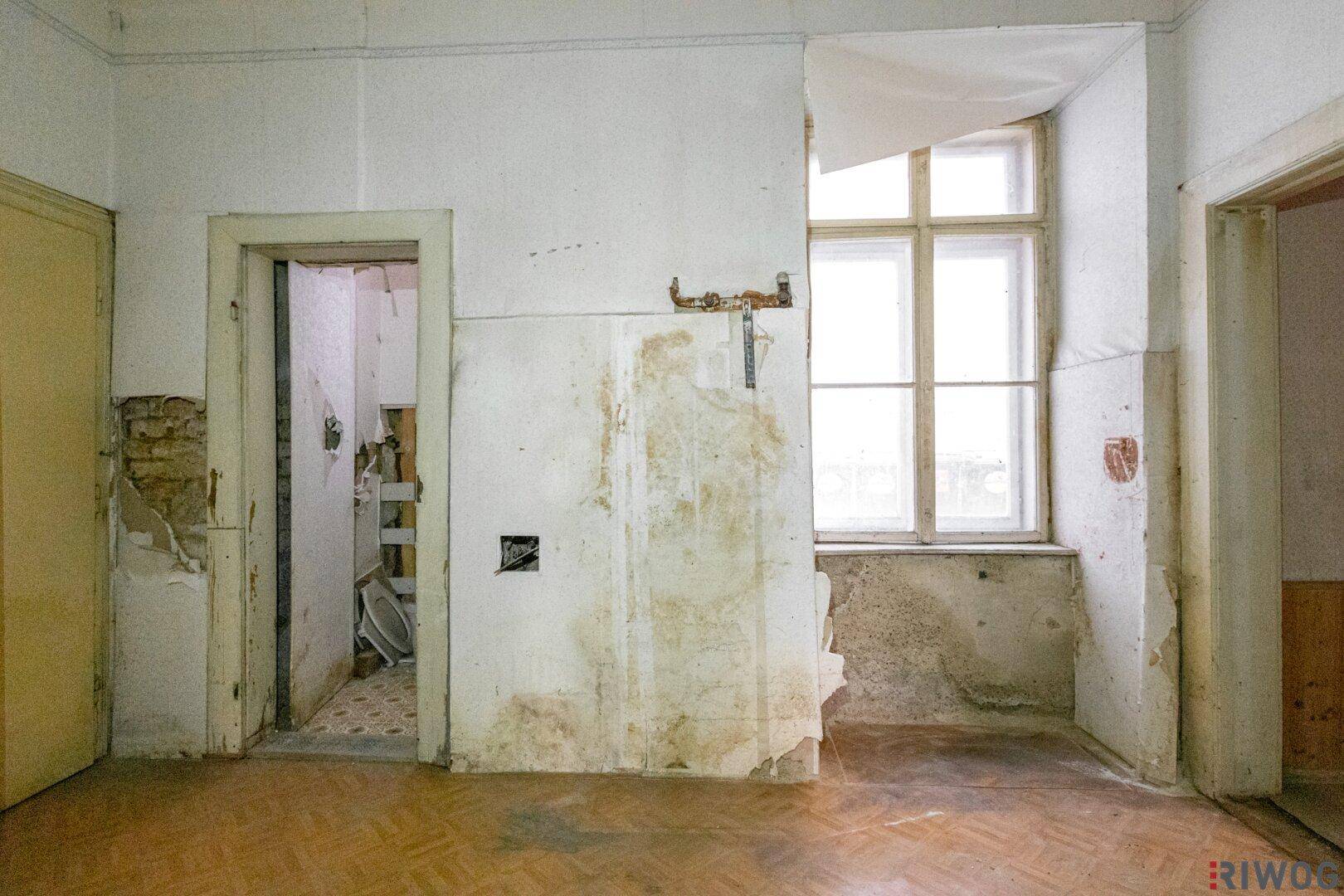 Renovierungsbedürftiger Raum mit altem Parkett und Blick auf einen Nebenraum.