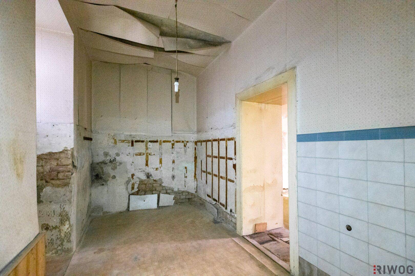 Sanierungsbedürftiger Raum mit Fliesenresten und freigelegten Wänden.