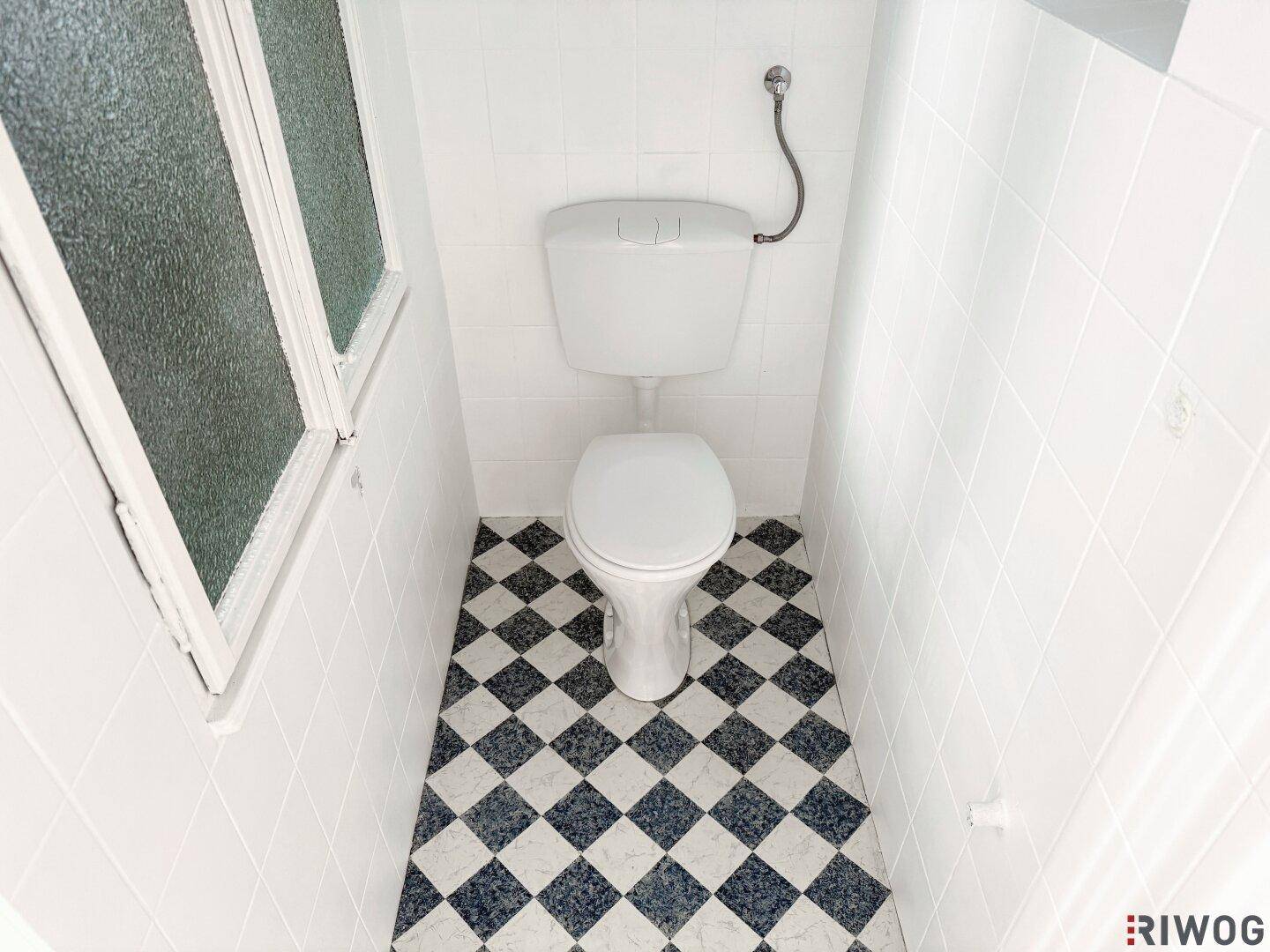 Separate Toilette mit Fenster und schwarz-weißem Schachbrettmuster-Boden, funktional.