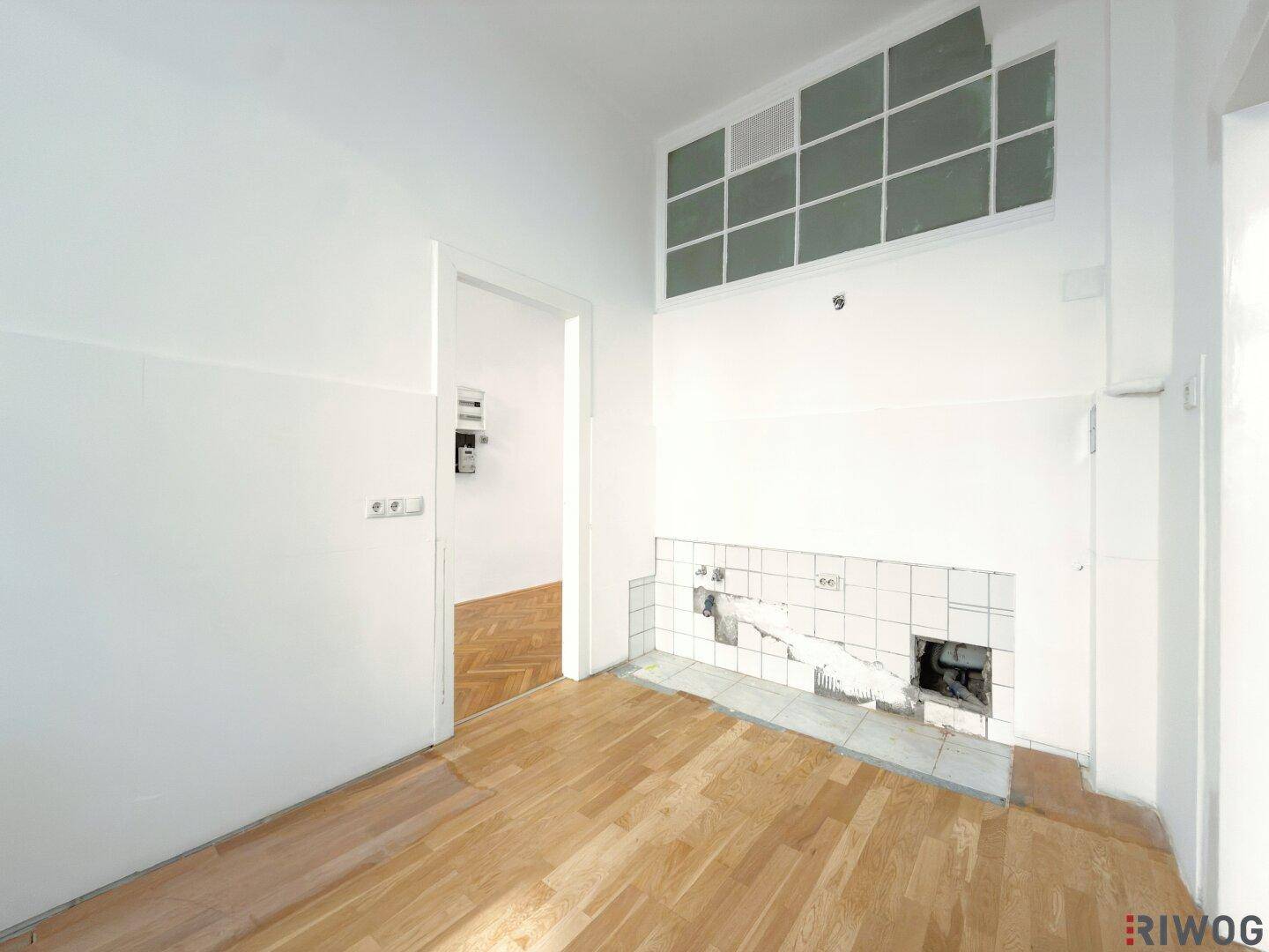 Leerer Küchenbereich mit Fliesenrückwand und Holzfußboden, bereit für neue Einrichtung.
