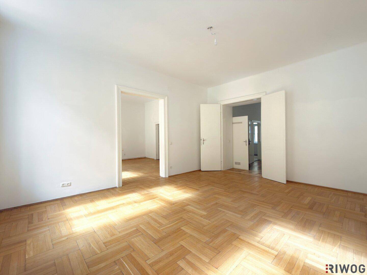 Geräumiges, leeres Zimmer mit Fischgrätparkett und hohen Decken, bereit zur Einrichtung.