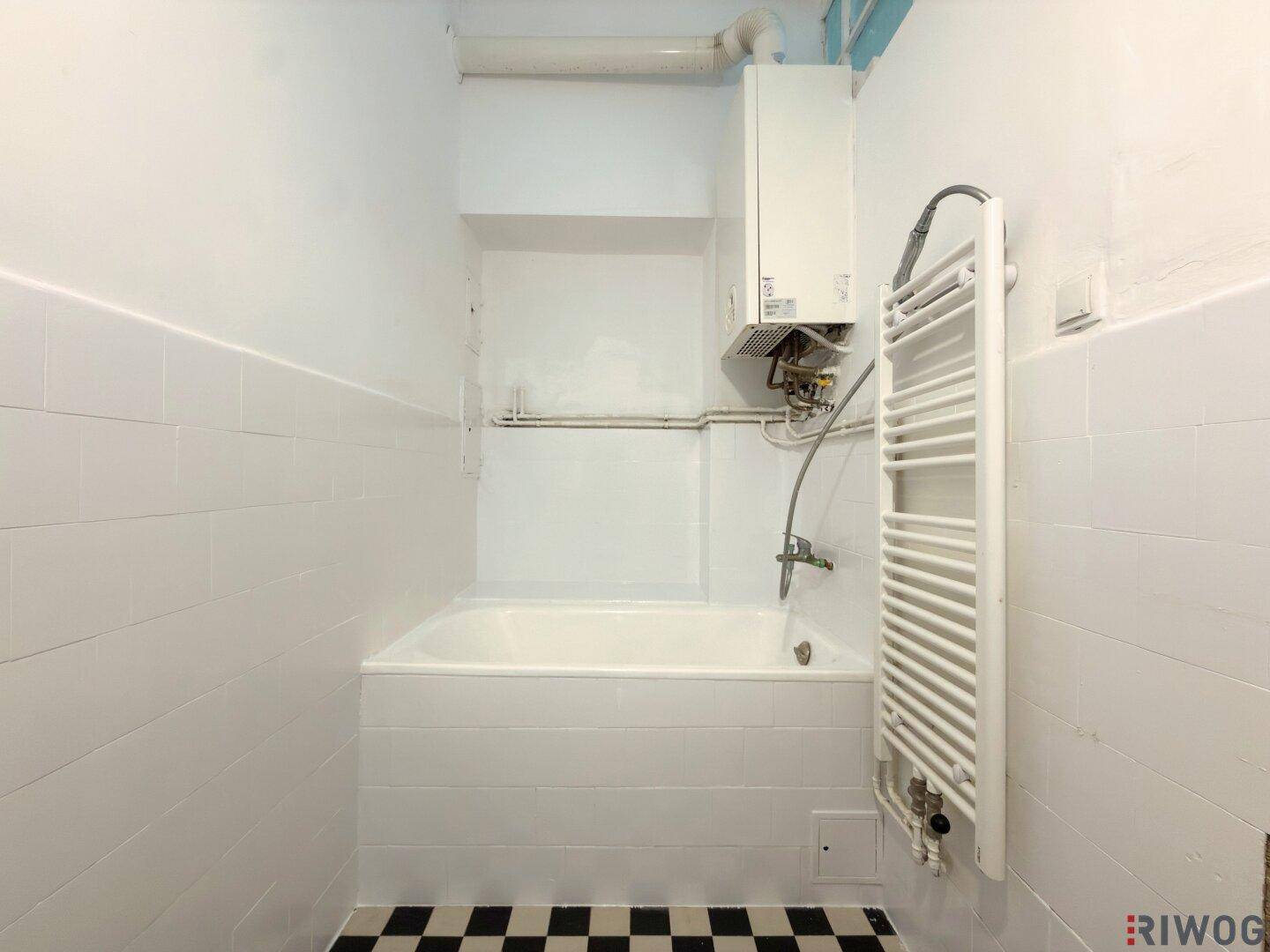 Badezimmer mit Badewanne, schwarz-weißem Schachbrettmuster-Boden und Heizkörper.