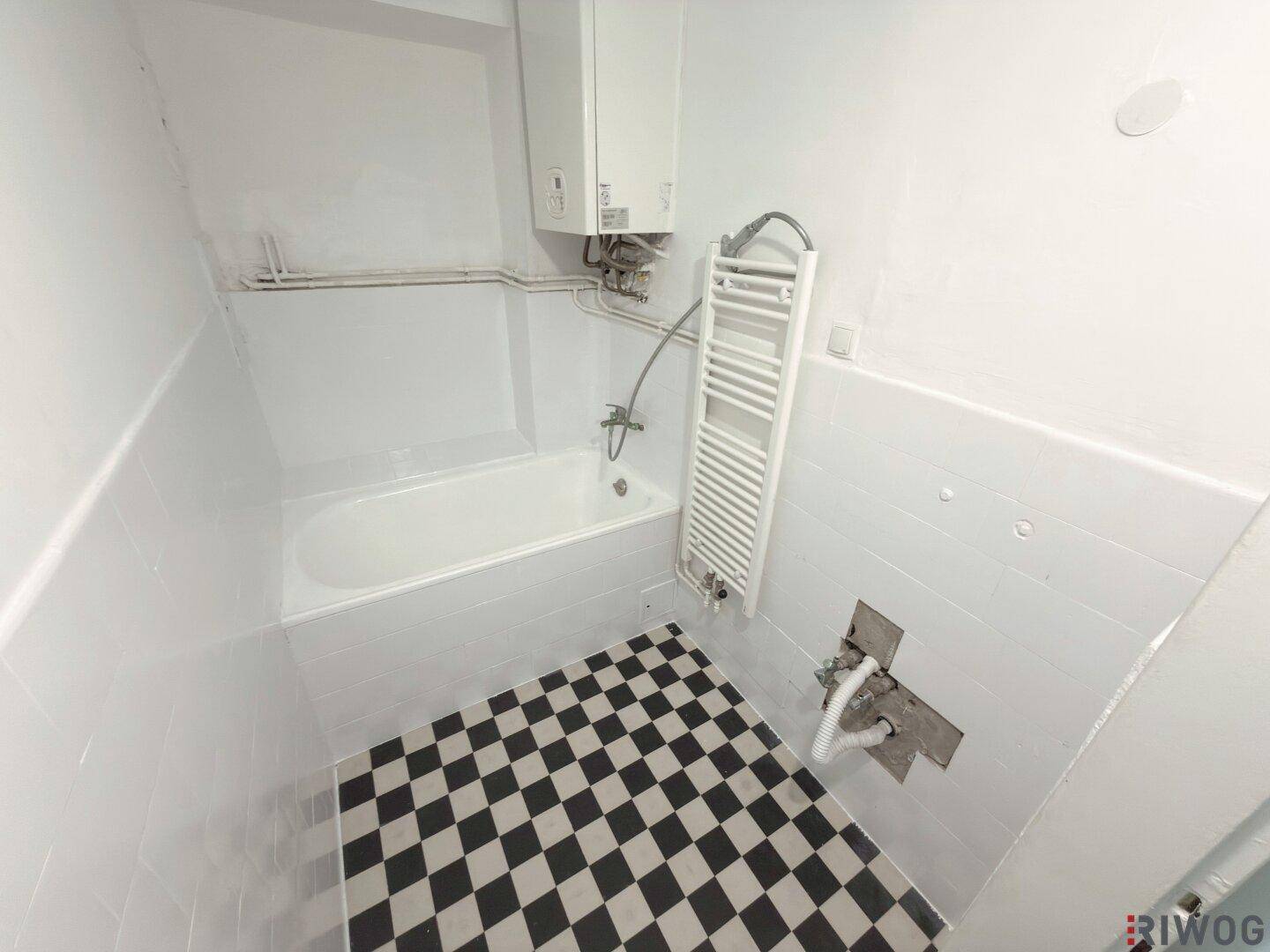 Badezimmer mit Badewanne, schwarz-weißem Schachbrettmuster-Boden und Heizkörper.