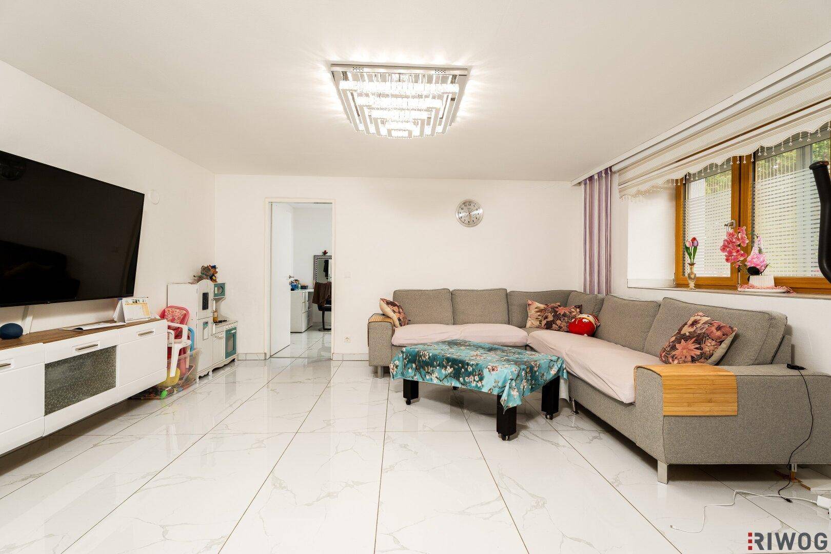 Großzügiges Wohnzimmer mit L-förmigem Sofa, Fliesenboden und einem modernen Deckenlicht.