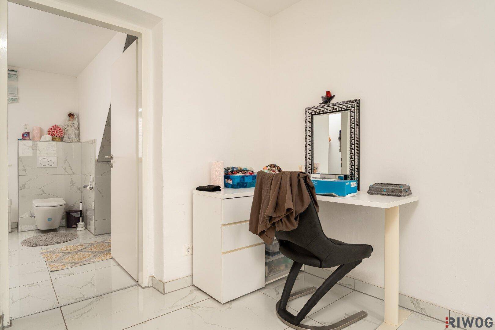 Schlafzimmer mit Schminktisch und offenem Zugang zu einem gefliesten Badezimmer.