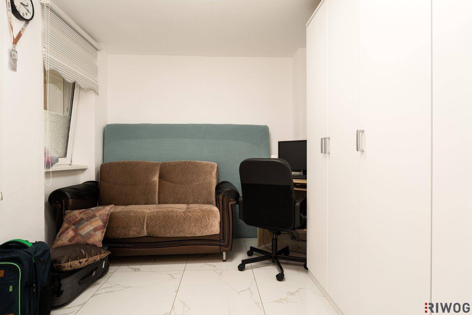 Funktionales Büro oder Gästezimmer mit weißem Kleiderschrank und kleinem Sofa.