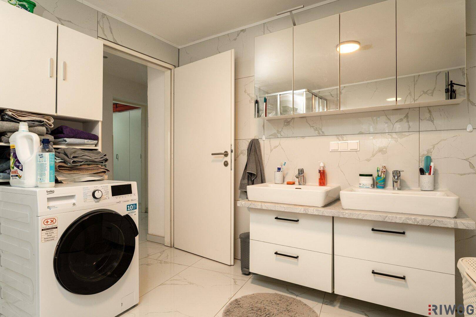 Badezimmer mit Waschmaschine, Doppelwaschbecken und Spiegelschrank für zusätzlichen Stauraum.