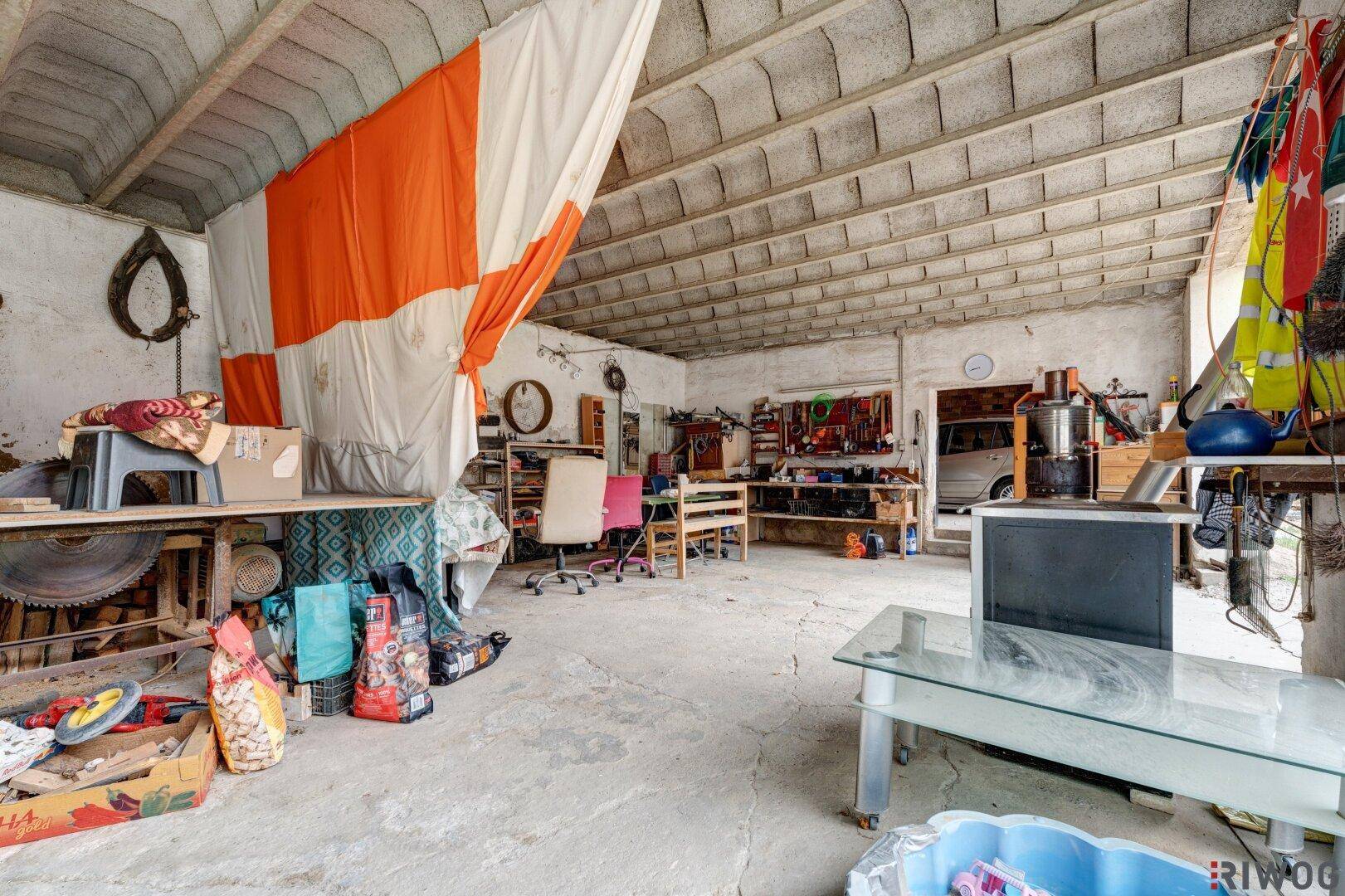 Geräumige Werkstatt oder Garage mit Betonboden, vielen Werkzeugen und einem Fahrzeug im Hintergrund.