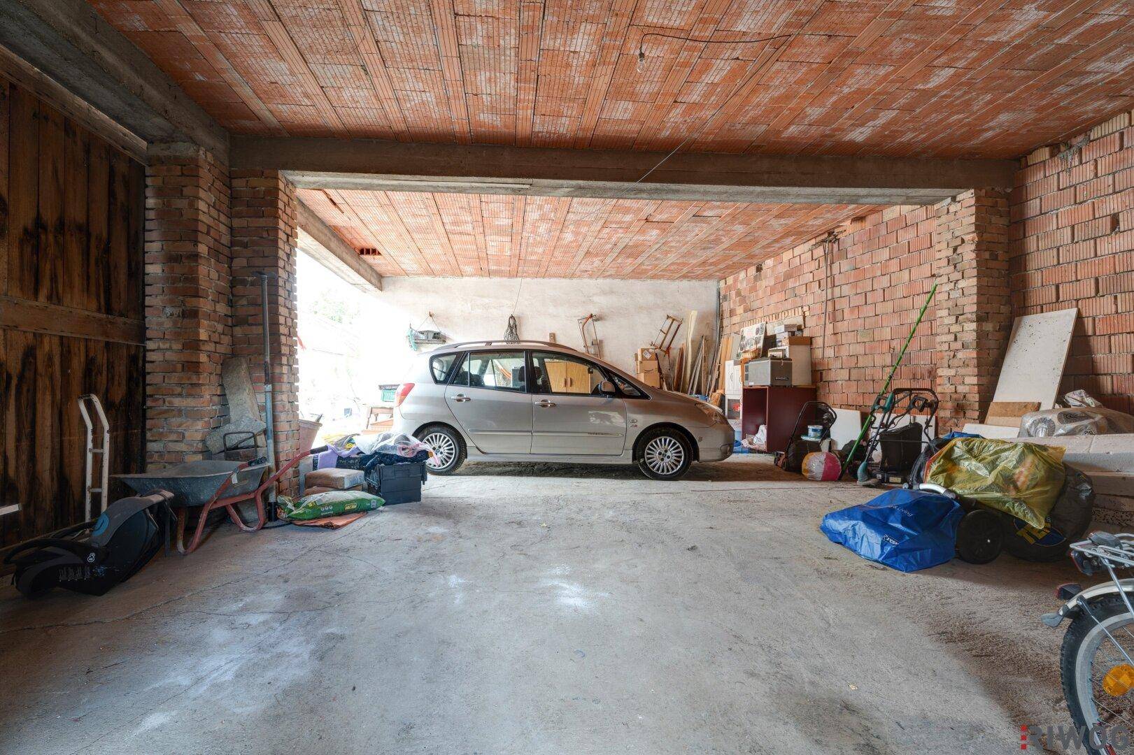 Große Garage mit einem geparkten Auto, unverputzten Ziegelwänden und einer Betondecke.
