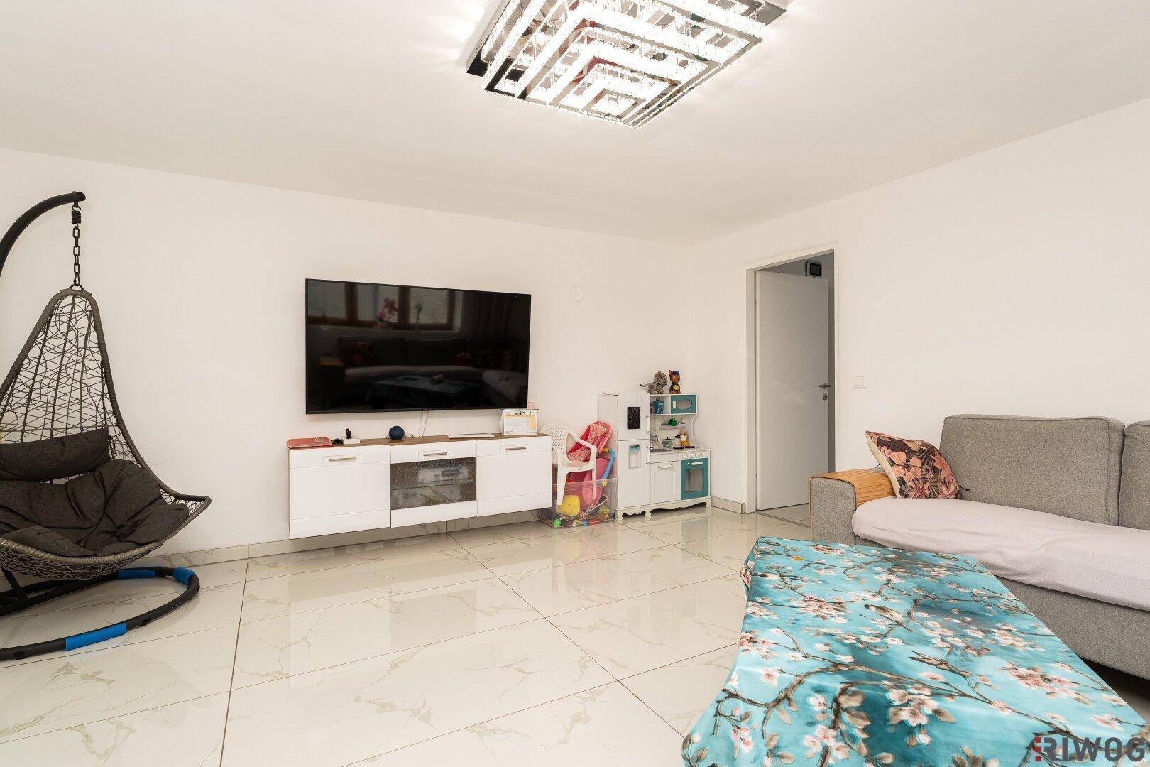 Geräumiges Wohnzimmer mit modernen Fliesen, großem Fernseher und einer gemütlichen Hängeschaukel.