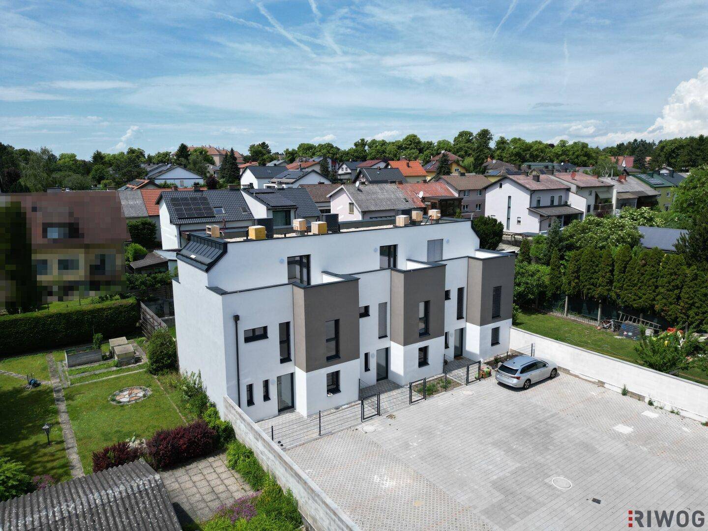 Moderne Reihenhäuser mit weißer und grauer Fassade, umgeben von viel Grün und Parkplätzen.
