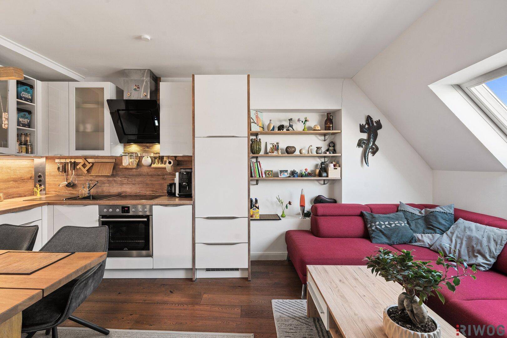 Moderne Einbauküche und gemütlicher Wohnbereich mit rotem Sofa unter Dachschrägen.