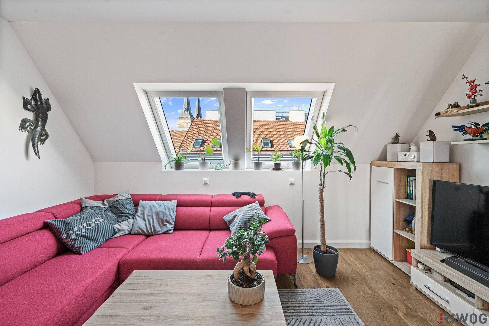Gemütliches Wohnzimmer mit rotem Ecksofa und hellen Dachfenstern mit Stadtblick.