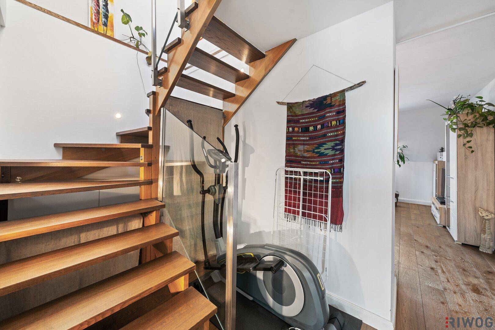 Elegante Holztreppe mit Glasgeländer und Fitnessgerät im Flurbereich.