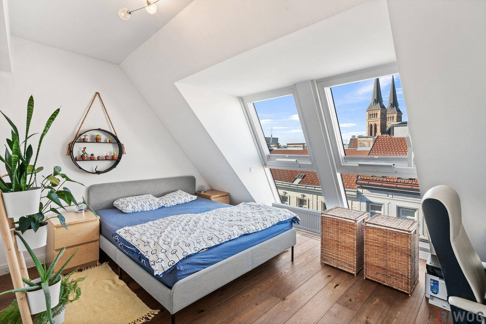 Helles Schlafzimmer mit Doppelbett, Holzboden und Dachfenstern mit Stadtblick.