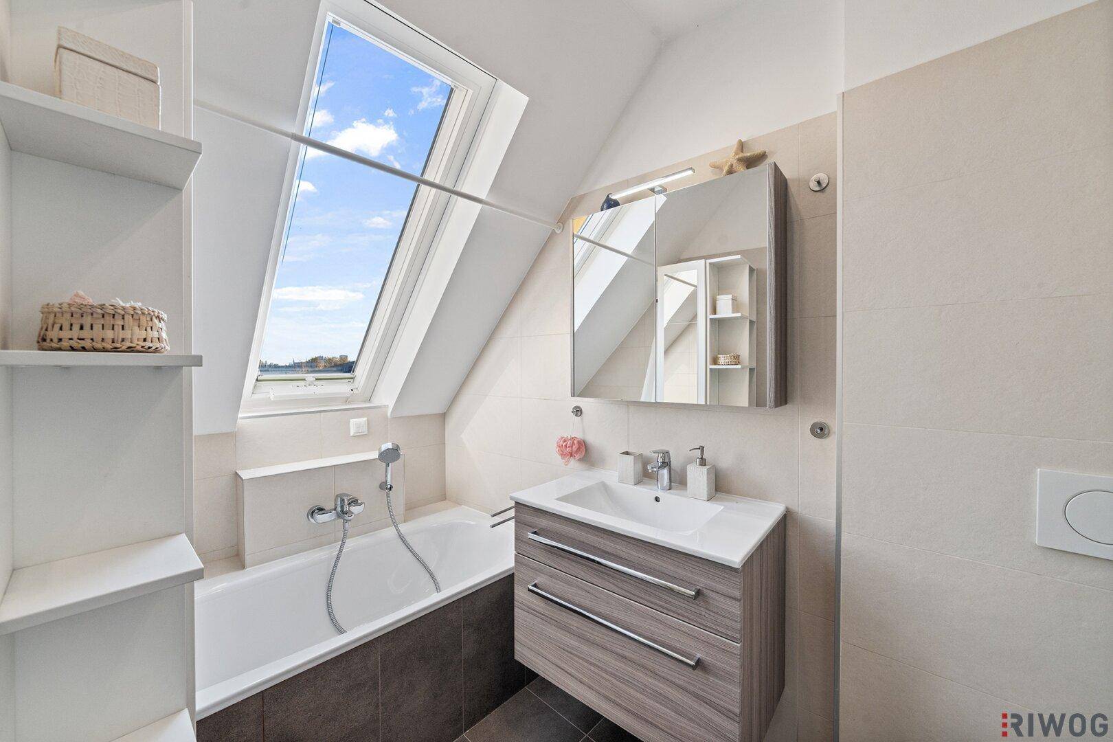Modernes Badezimmer mit Badewanne, Waschtisch und großem Dachfenster für viel Licht.