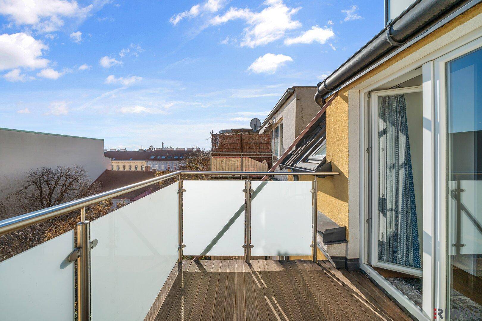 Kleiner Balkon mit Holzdeck und Glasgeländer, zugänglich vom Innenbereich.
