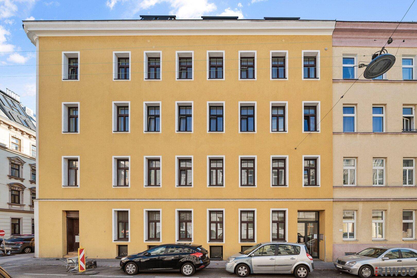 Gelbe Fassade eines Mehrfamilienhauses mit vielen Fenstern an einer Stadtstraße.