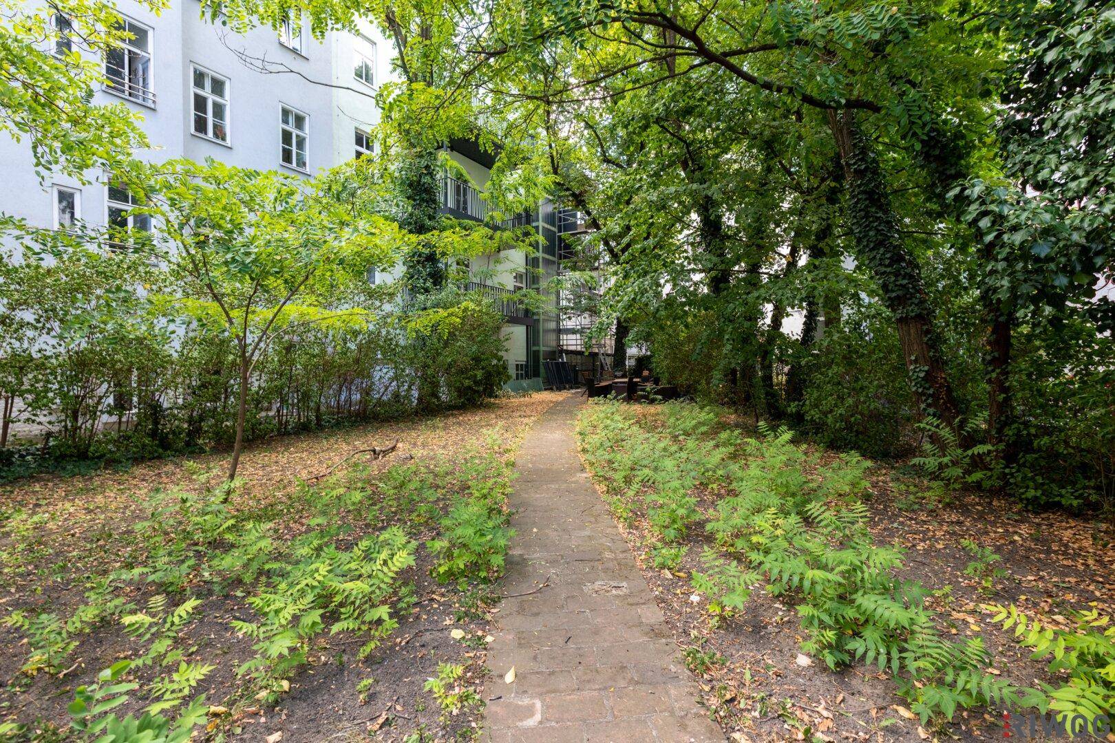 Gepflegter Gartenbereich mit einem Weg, umgeben von Bäumen und Sträuchern, im Hinterhof des Gebäudes.