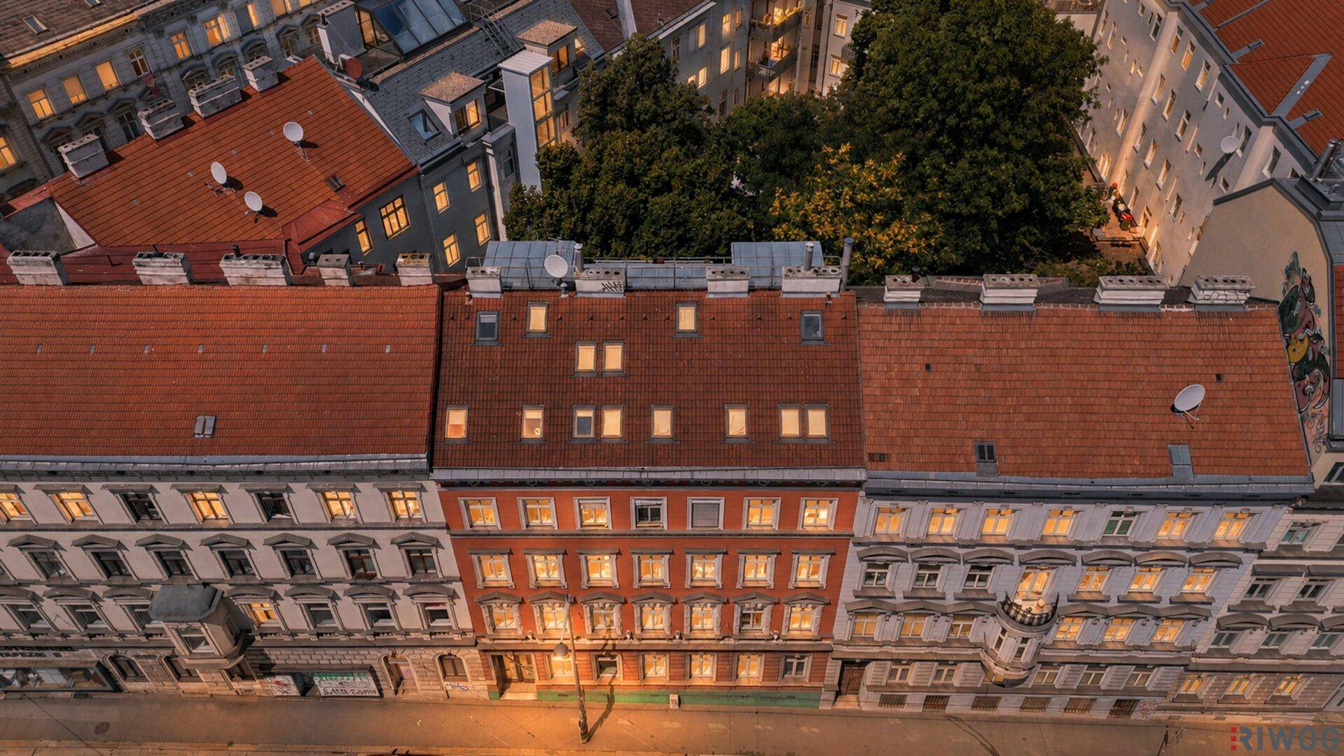 Beleuchtete Fassaden von Stadthäusern entlang einer Straße bei Einbruch der Dunkelheit.