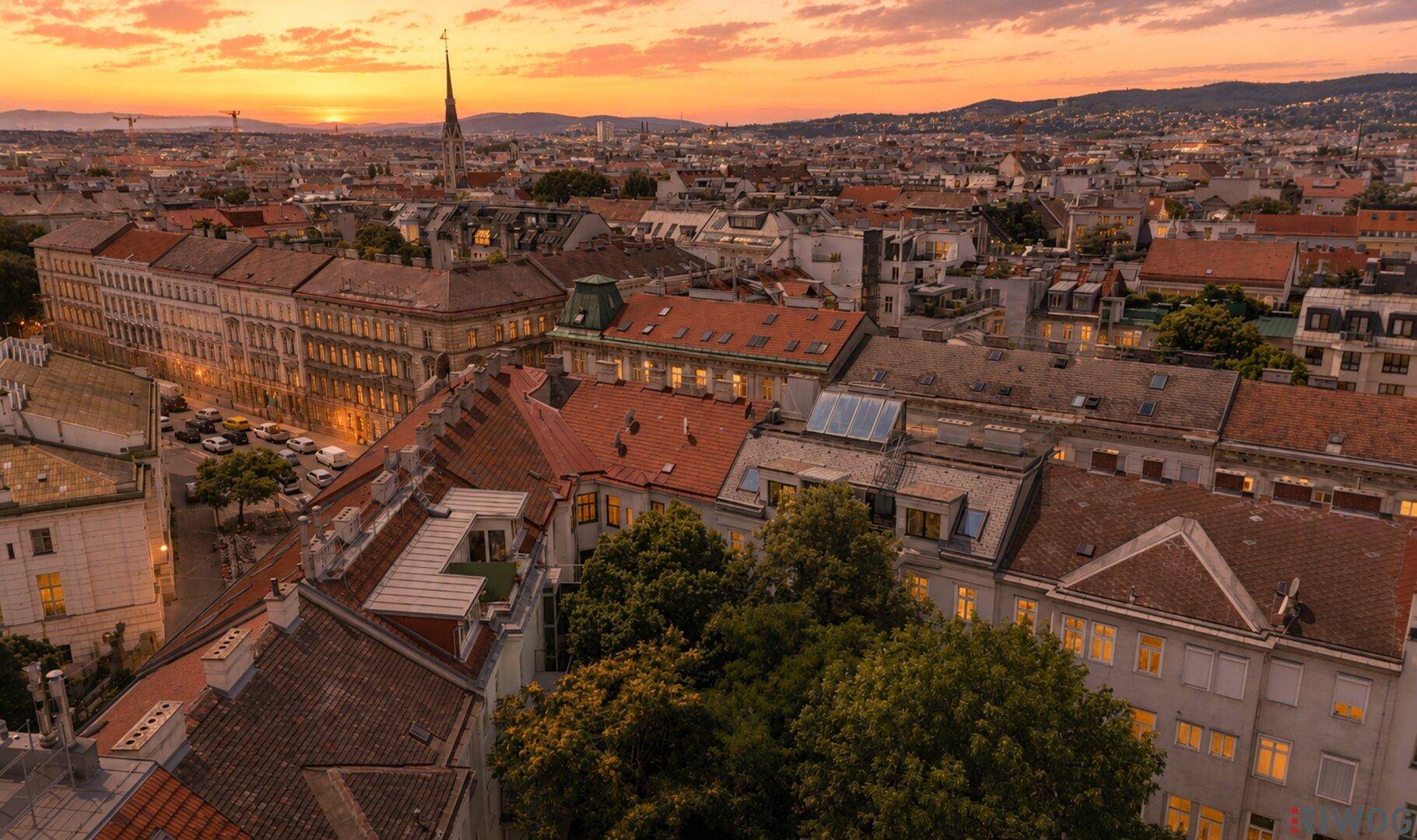 Panoramablick über eine Stadtlandschaft bei Sonnenuntergang mit roten Dächern und Bergen im Hintergrund.