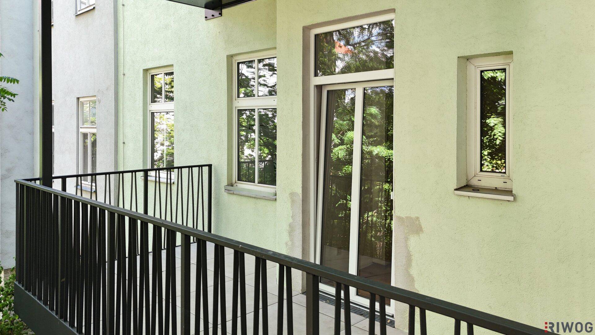 Balkon mit schwarzem Geländer und Blick auf die hellgrüne Fassade mit Fenstern und Balkontür.