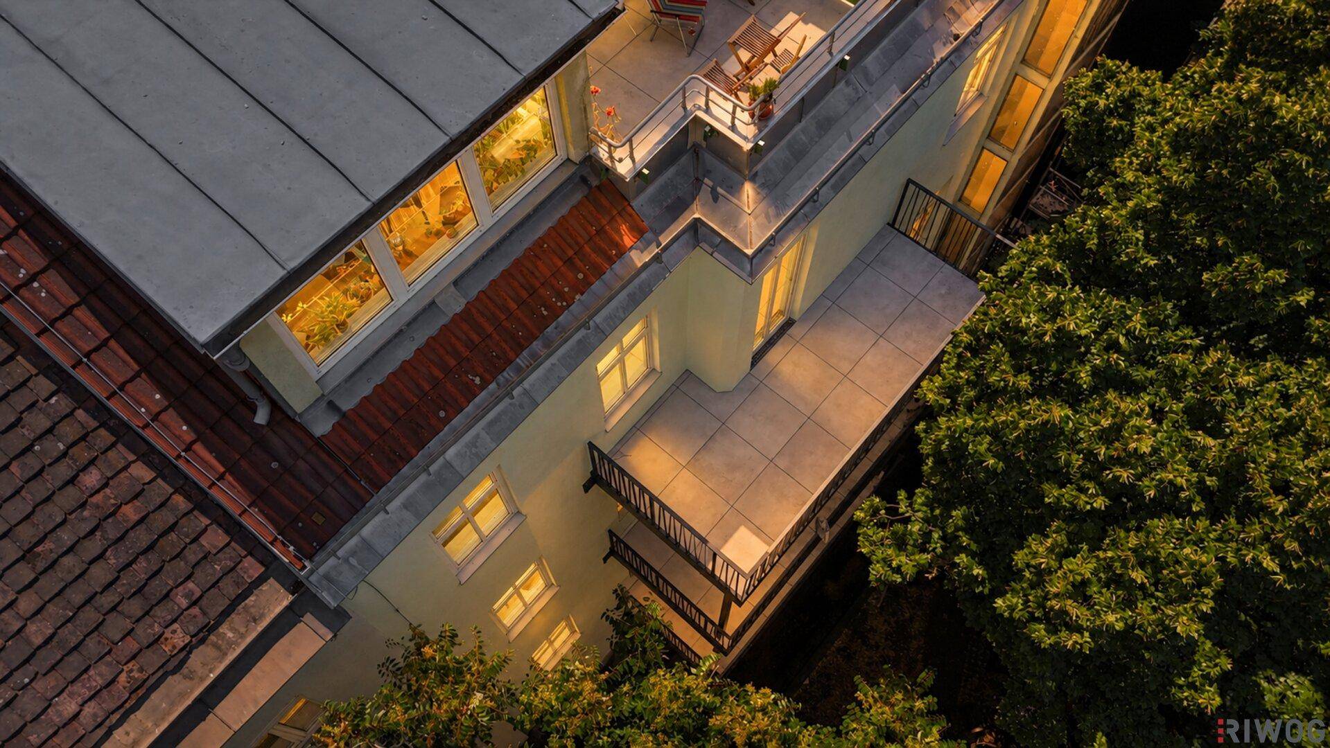 Luftaufnahme des Gebäudes bei Dämmerung mit beleuchteten Fenstern und einer Dachterrasse.