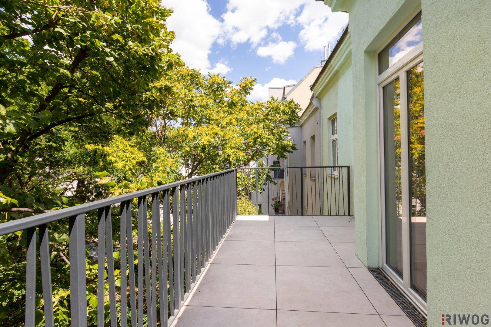 Heller Balkon mit Fliesenboden und schlichtem Geländer, bietet einen ruhigen Blick auf die umliegenden Bäume.