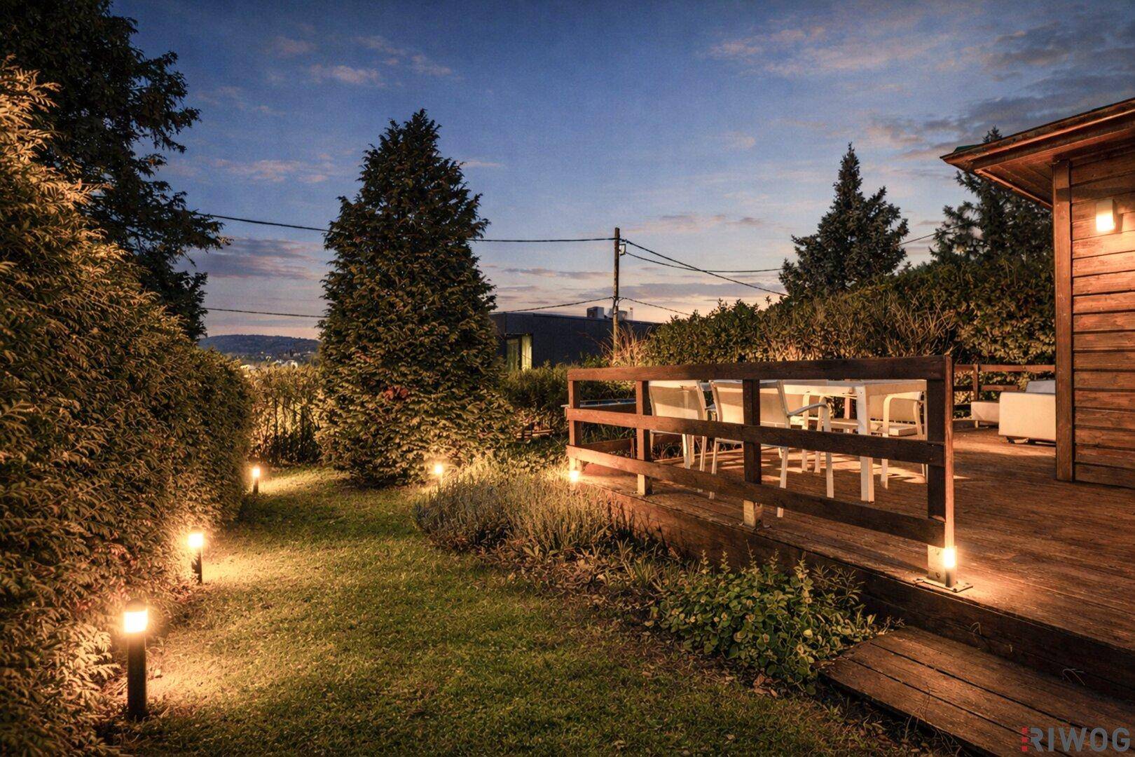 Beleuchteter Gartenbereich und Holzterrasse bei Nacht, schaffen eine gemütliche Atmosphäre.