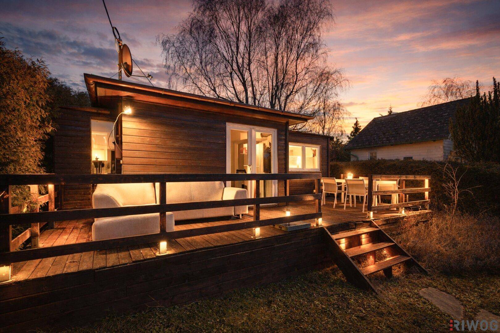 Gemütliche Abendstimmung auf der Holzterrasse mit beleuchtetem Haus und Garten.