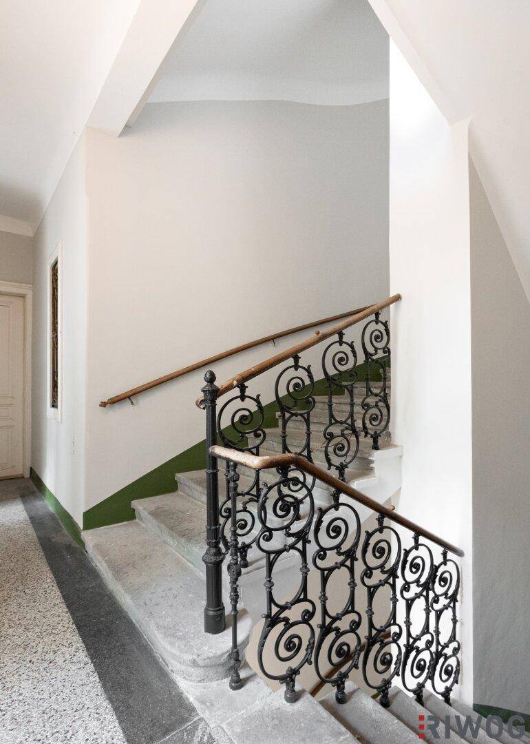 Elegantes Treppenhaus mit schmiedeeisernem Geländer, Steinstufen und hohen Decken in einem Altbau.