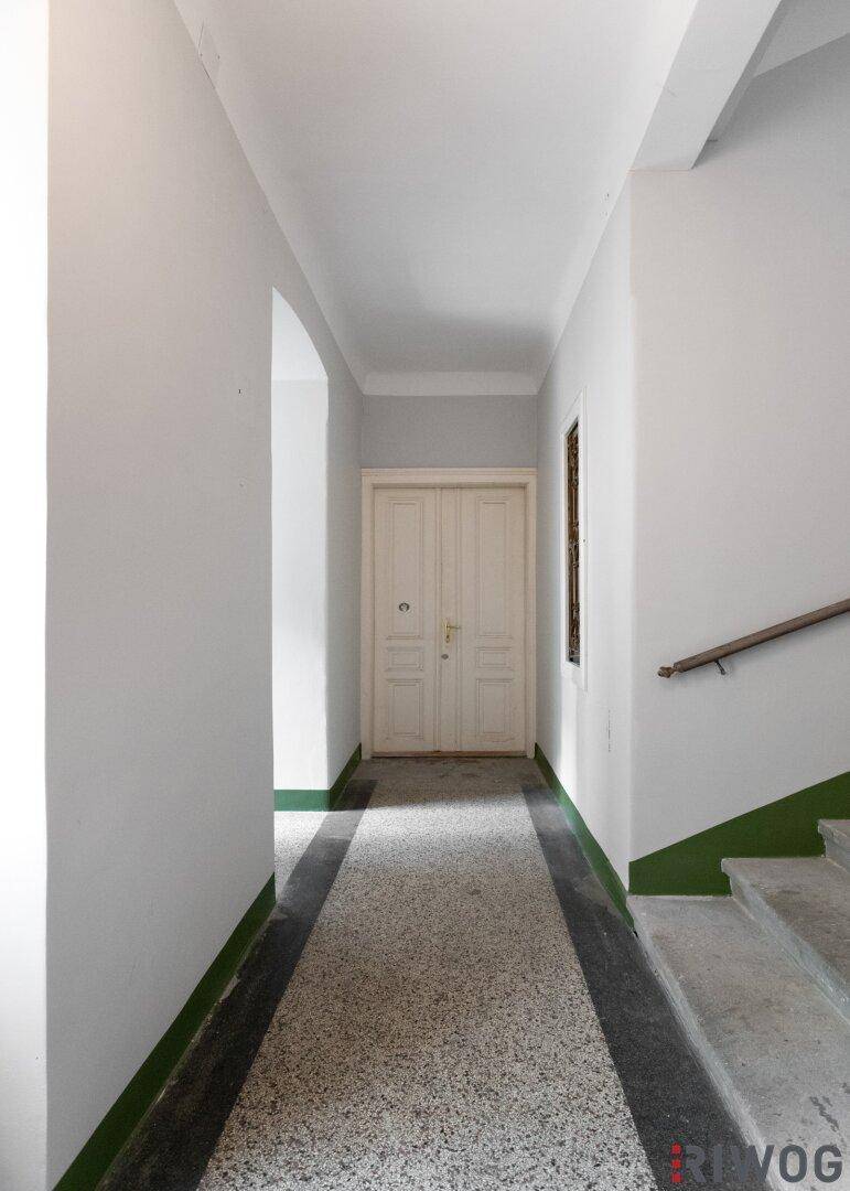 Heller Flur mit Terrazzoboden, hohen Decken und einer Doppeltür am Ende des Ganges.