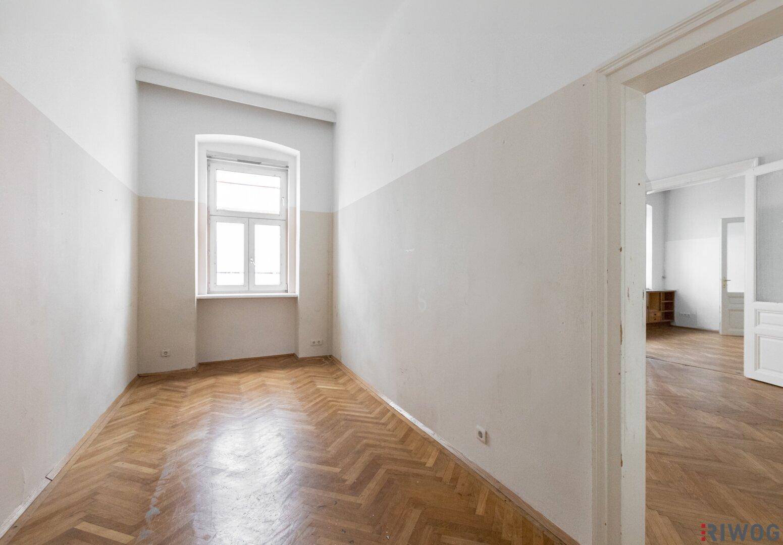 Helles Zimmer mit Fischgrätparkett und einem großen Fenster, ideal als Schlafzimmer oder Büro.