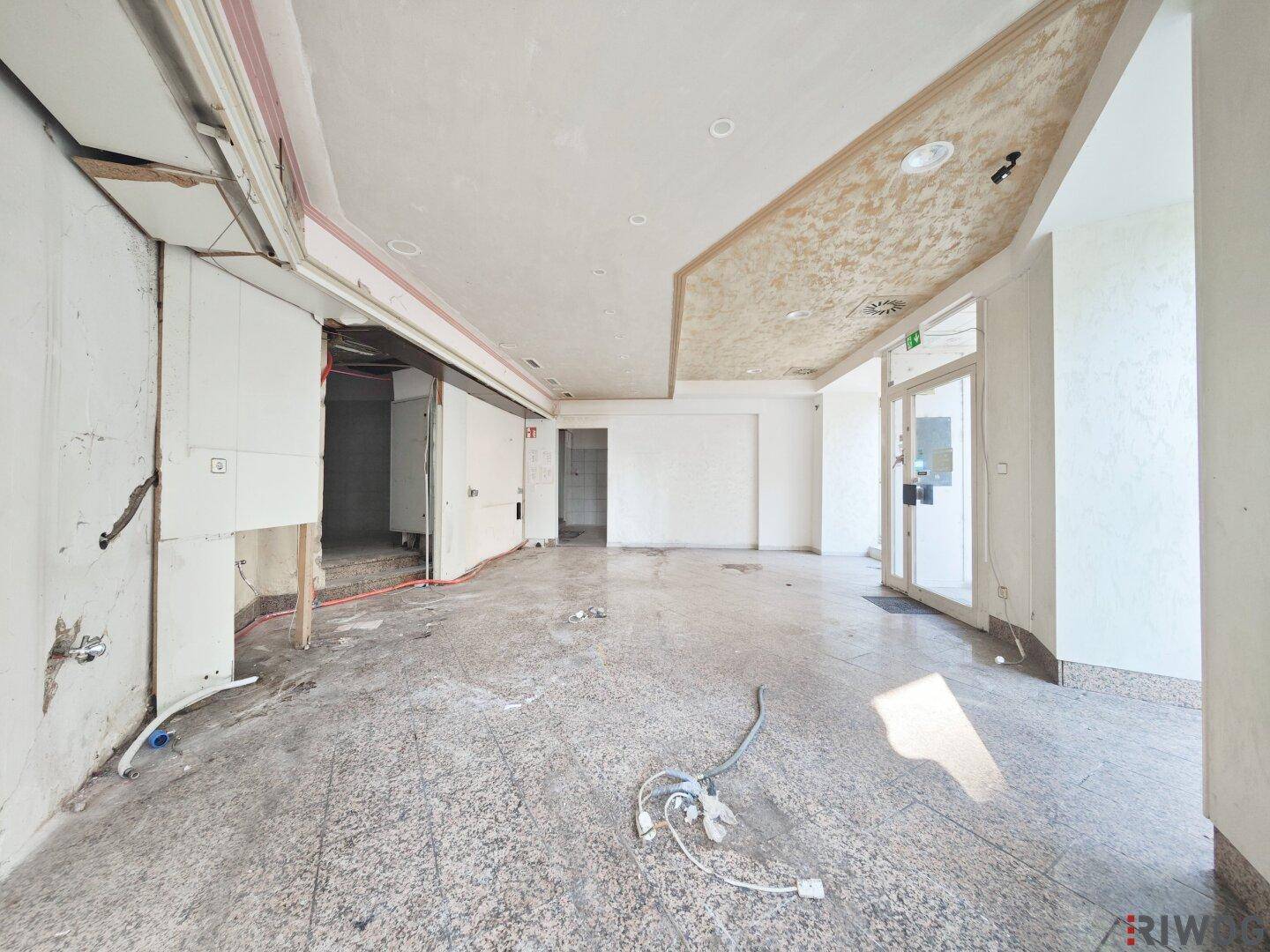 Geräumiger, unmöblierter Geschäftsraum mit Fliesenboden und sichtbaren Installationsresten, bereit zur Neugestaltung.