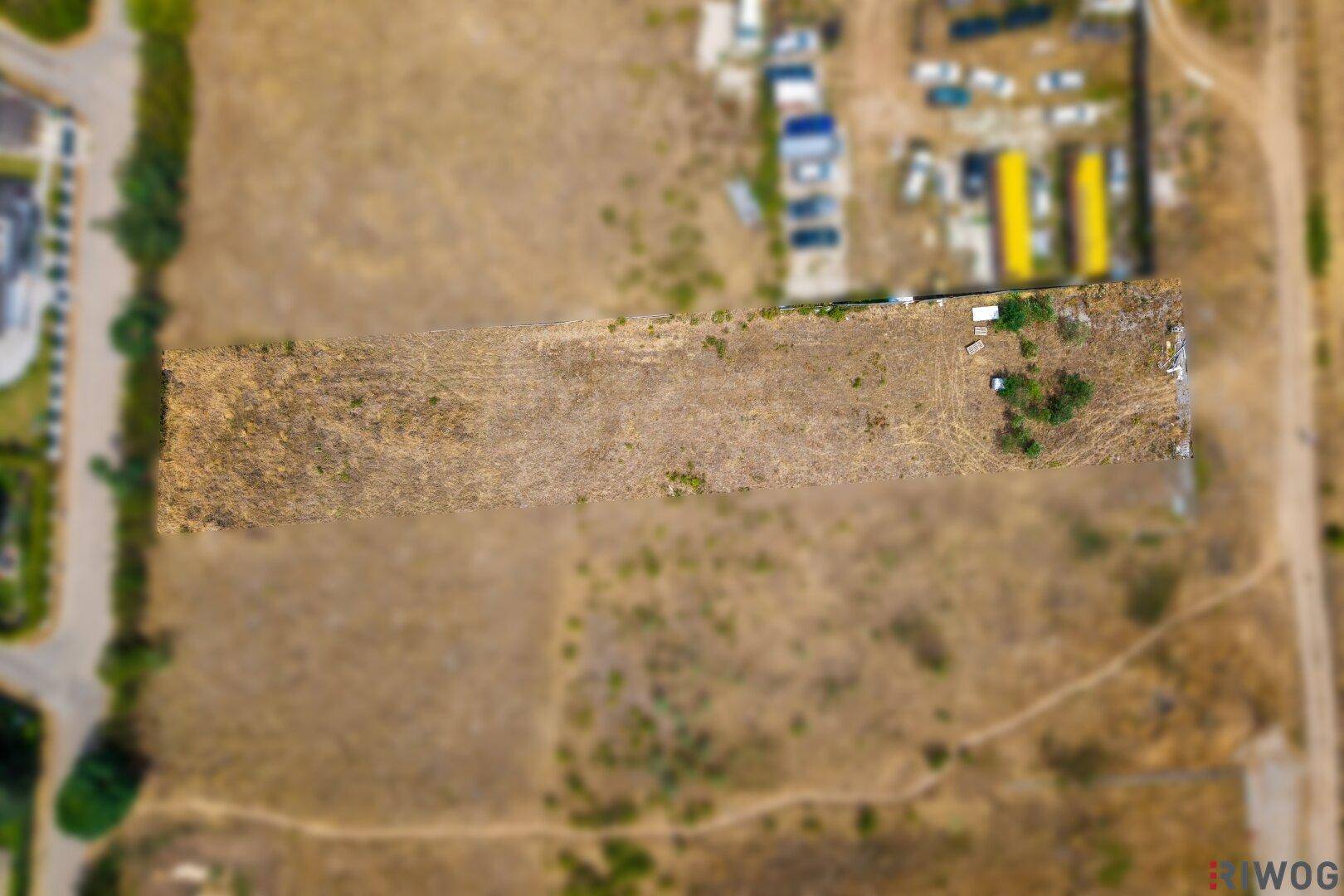 Senkrechte Luftaufnahme eines langen, schmalen unbebauten Landstreifens mit trockener Vegetation.
