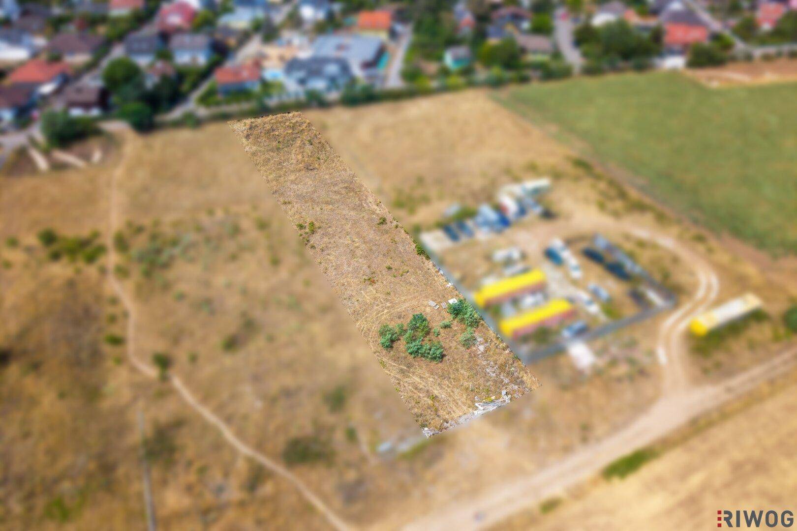 Luftaufnahme eines unbebauten Grundstücks mit trockener Erde und Gras, umgeben von einer ländlichen Umgebung.