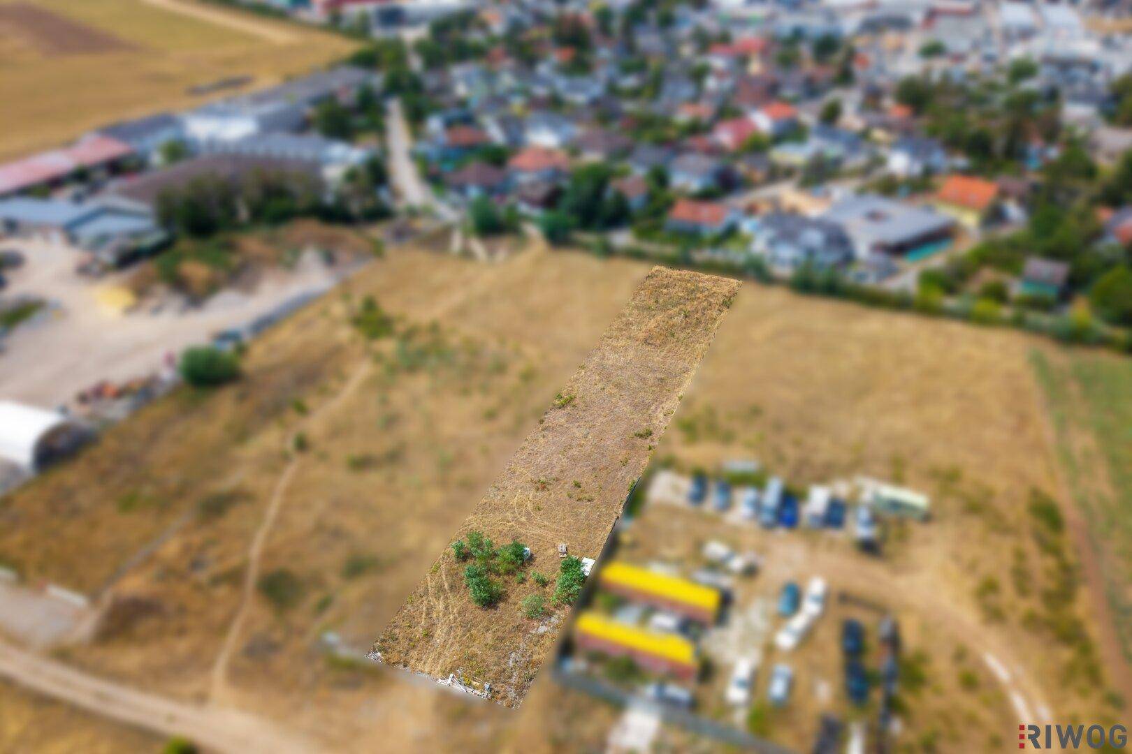 Luftaufnahme eines unbebauten Grundstücks mit trockener Erde und Gras, umgeben von einer ländlichen Umgebung.