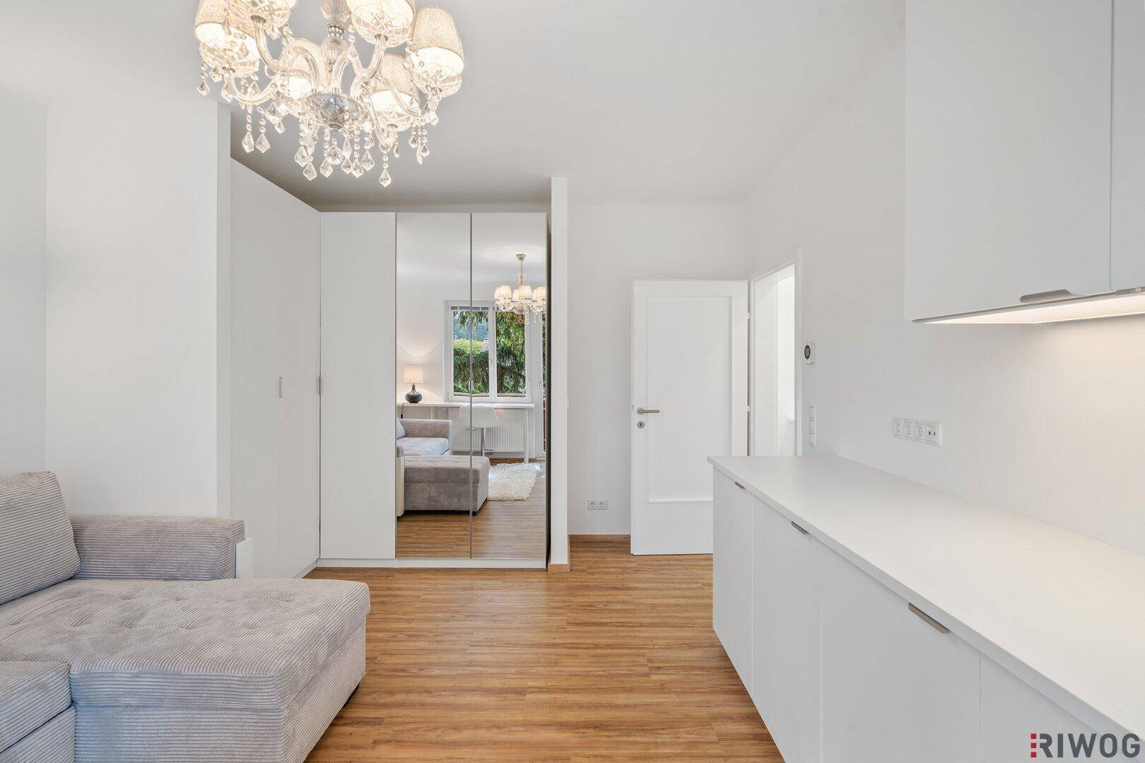 Heller Wohnraum mit Sofa, Spiegelschrank und Blick auf die Küchenzeile.