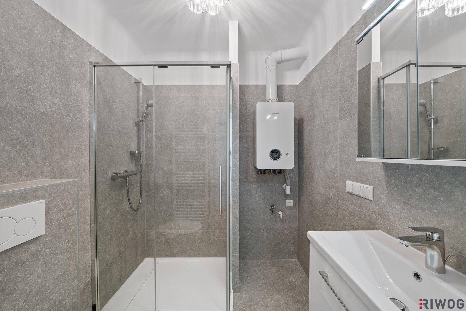Modernes Badezimmer mit grauen Fliesen, Duschkabine, Waschbecken und Warmwasserbereiter.